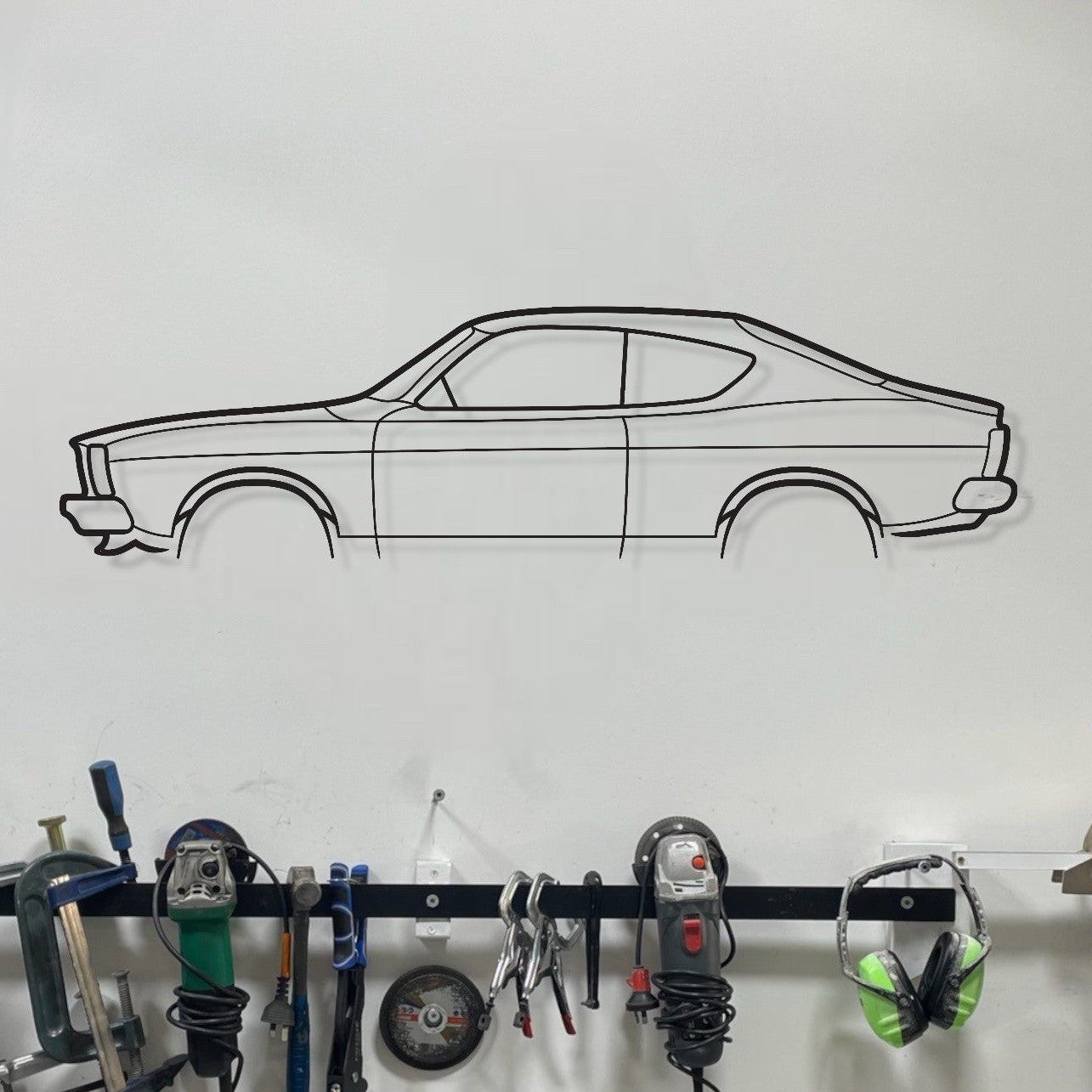 Garage wall with tools hanging on a rack and a car outline on the wall.
