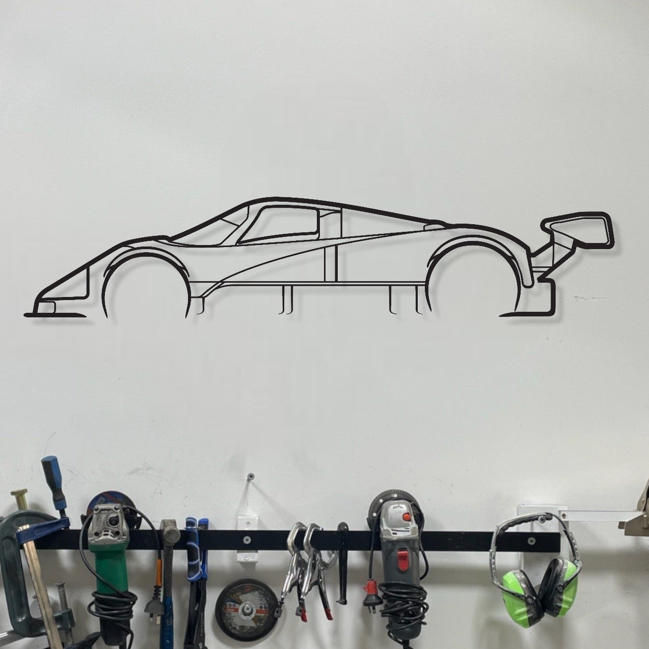 Wall-mounted tool rack with automotive tools and a car-shaped decal on a white wall.