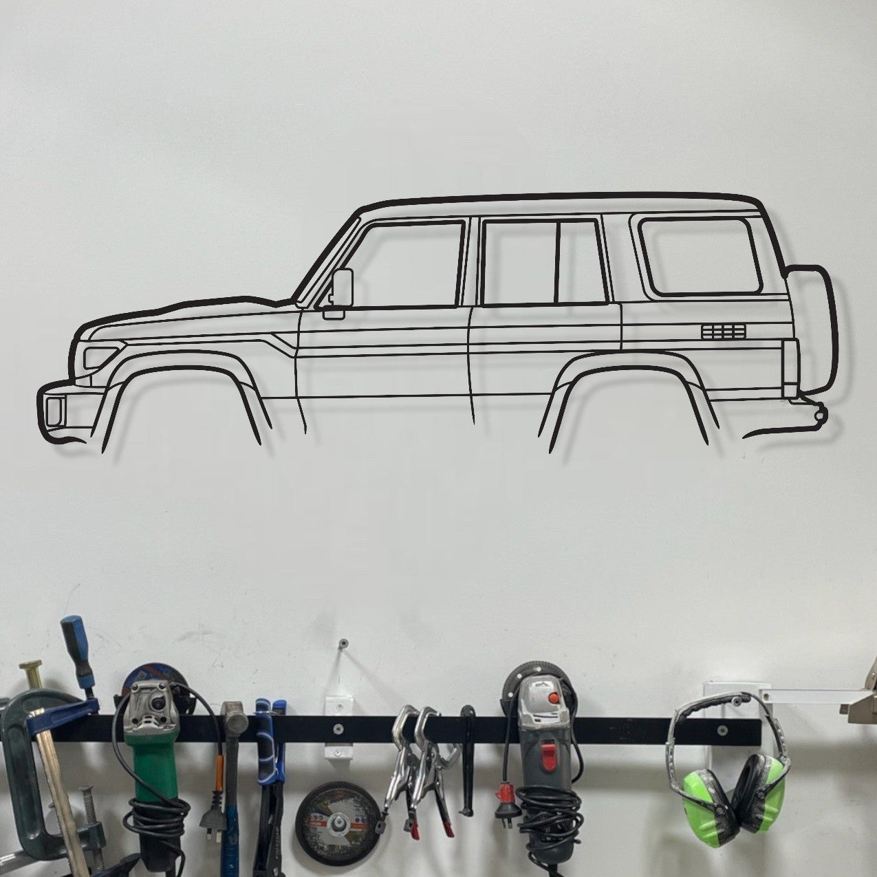 Wall-mounted tool rack with various tools and a car decal on a white wall.