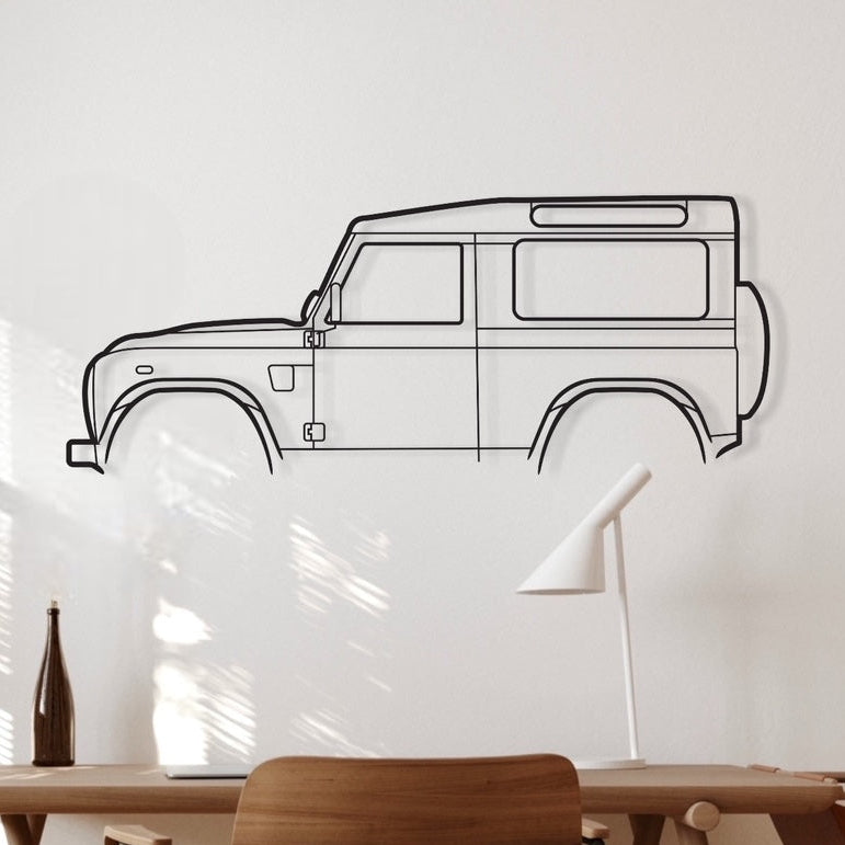 A metal wall art depicting the silhouette of a Land Rover Defender 2016 car, displayed on a wall above a desk with chairs and a lamp.