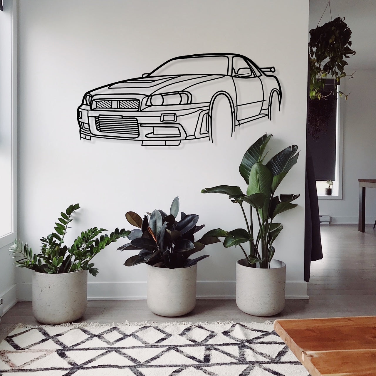 A wall-mounted silhouette of a Nissan Skyline R34 GTR car above three potted plants in a home setting.