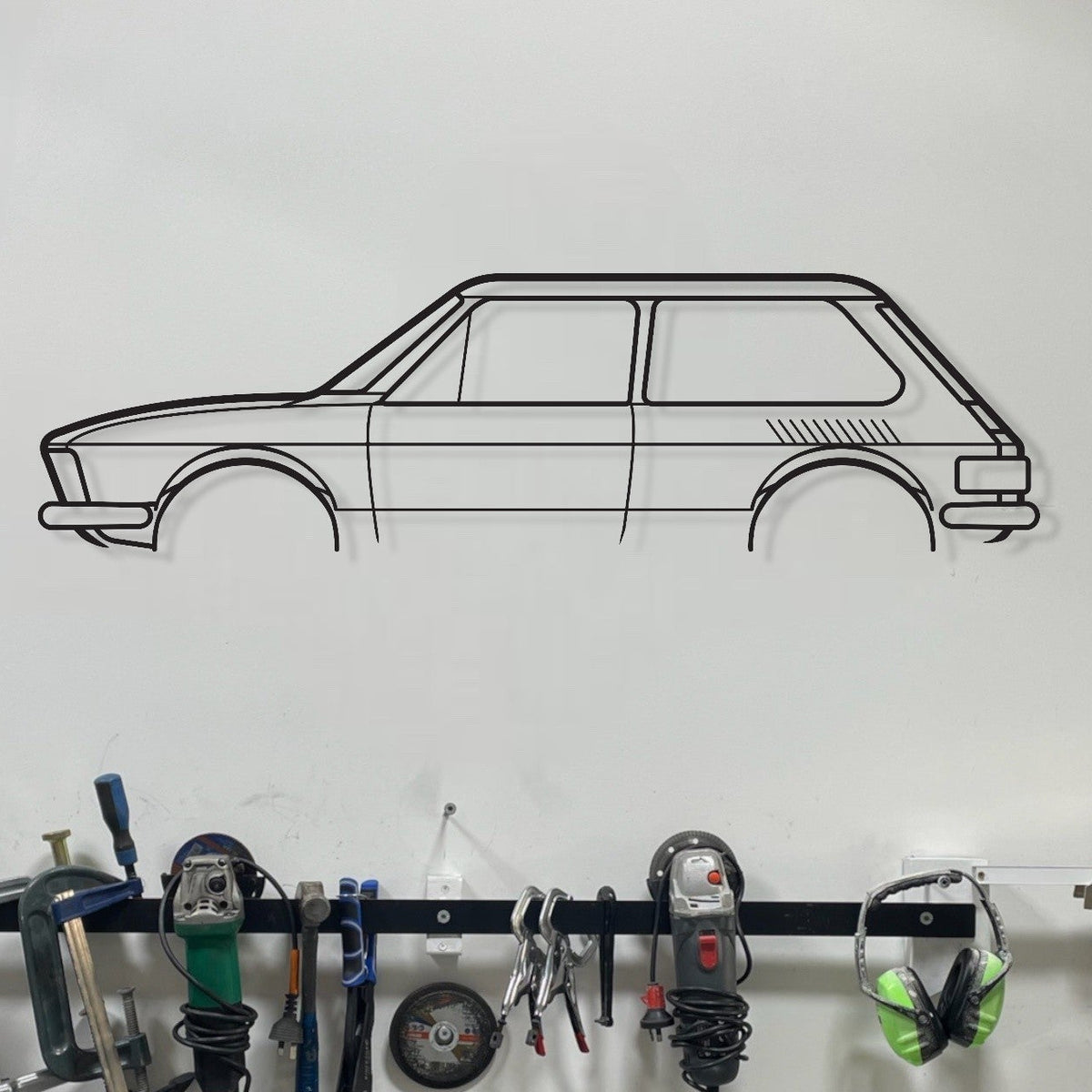 Wall-mounted tool rack with various tools and a car illustration on a white wall.