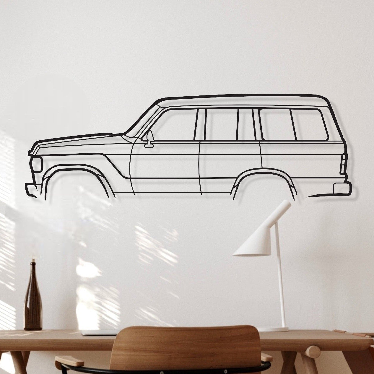 Wooden desk with chair against a white wall with a black line drawing of a car.