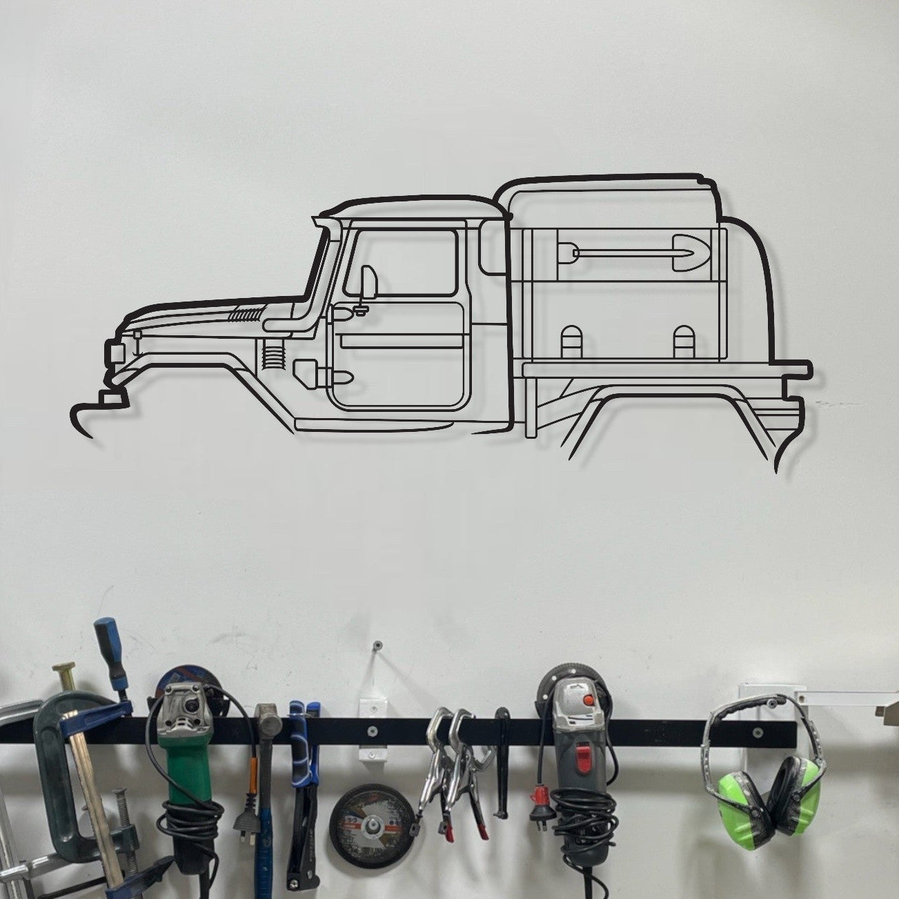 Wall-mounted tool rack with various tools in a workshop setting, featuring a black and white illustration of a truck above.