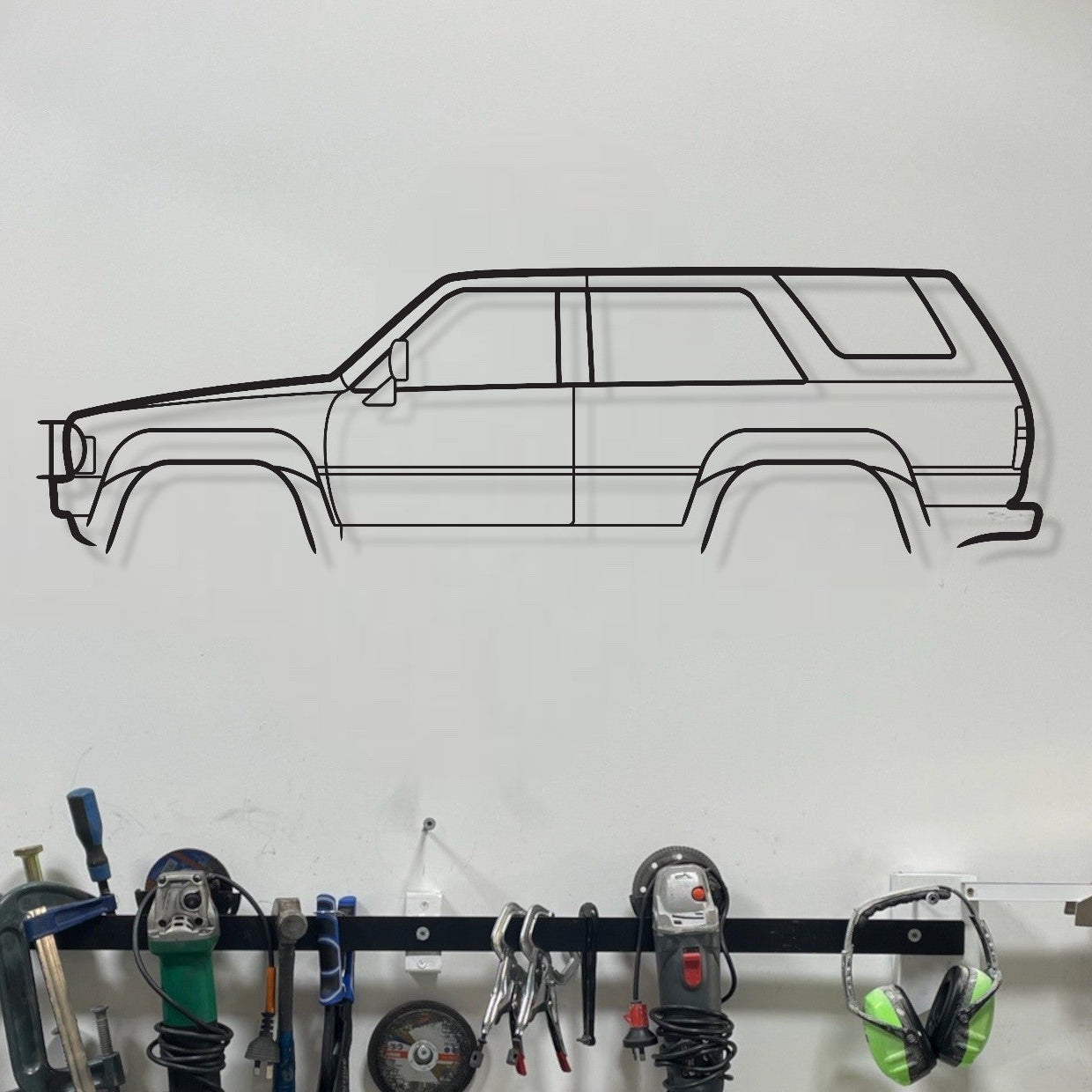 Wall-mounted tool rack with various tools and a car outline on a white wall.