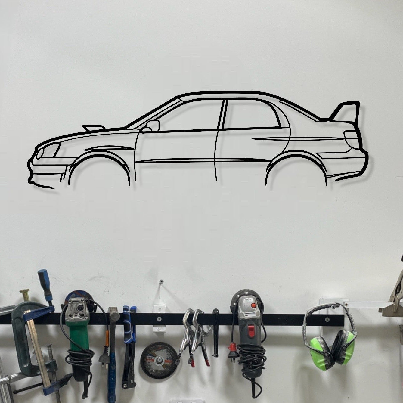 Garage wall with tools hanging on a rack, car decal, and workbench.