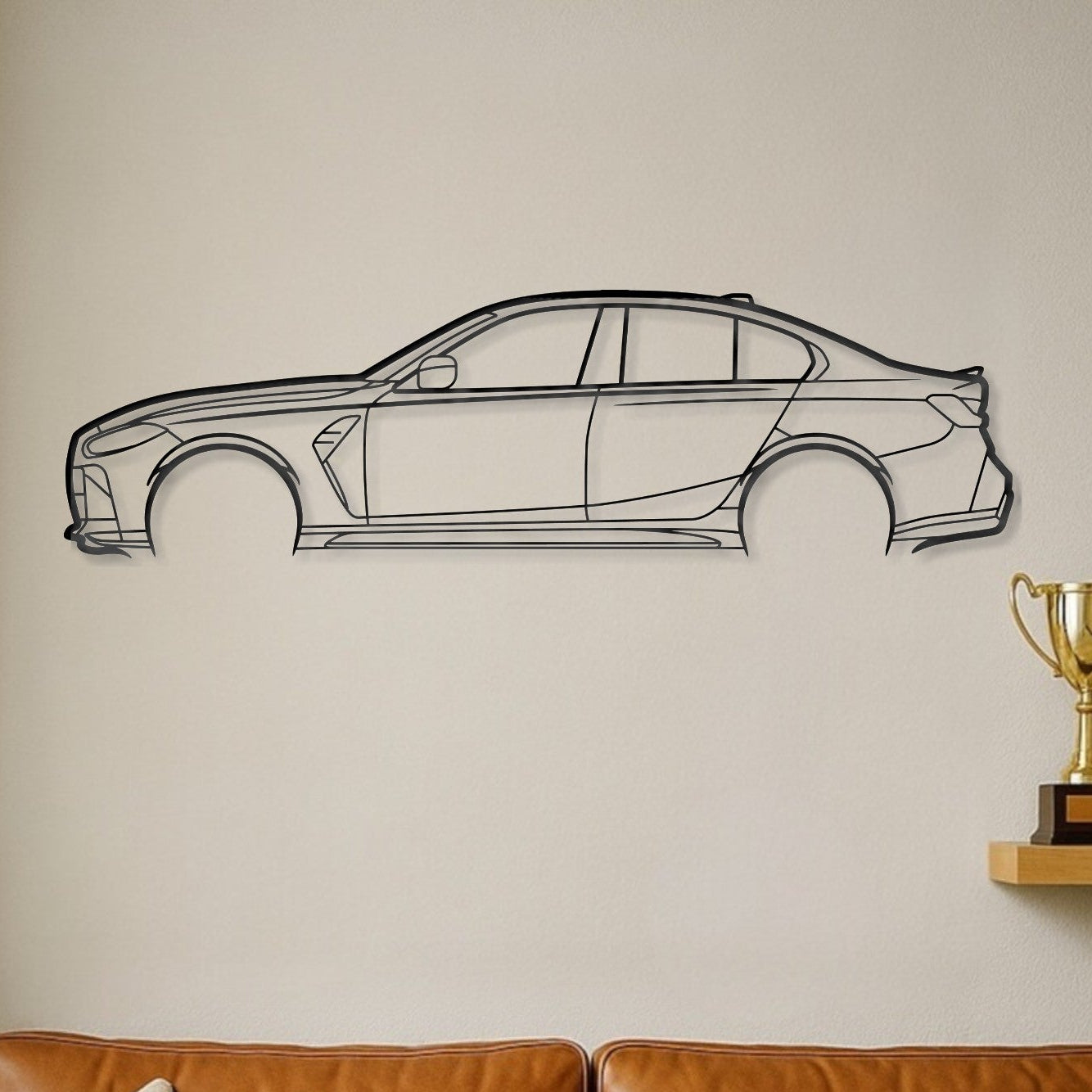 A black steel car silhouette wall decal is displayed on a beige wall above a brown leather sofa with two cream pillows, next to a wooden shelf holding two gold trophies.