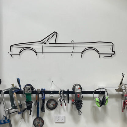 Wall-mounted tool rack with various tools and a car outline on the wall.