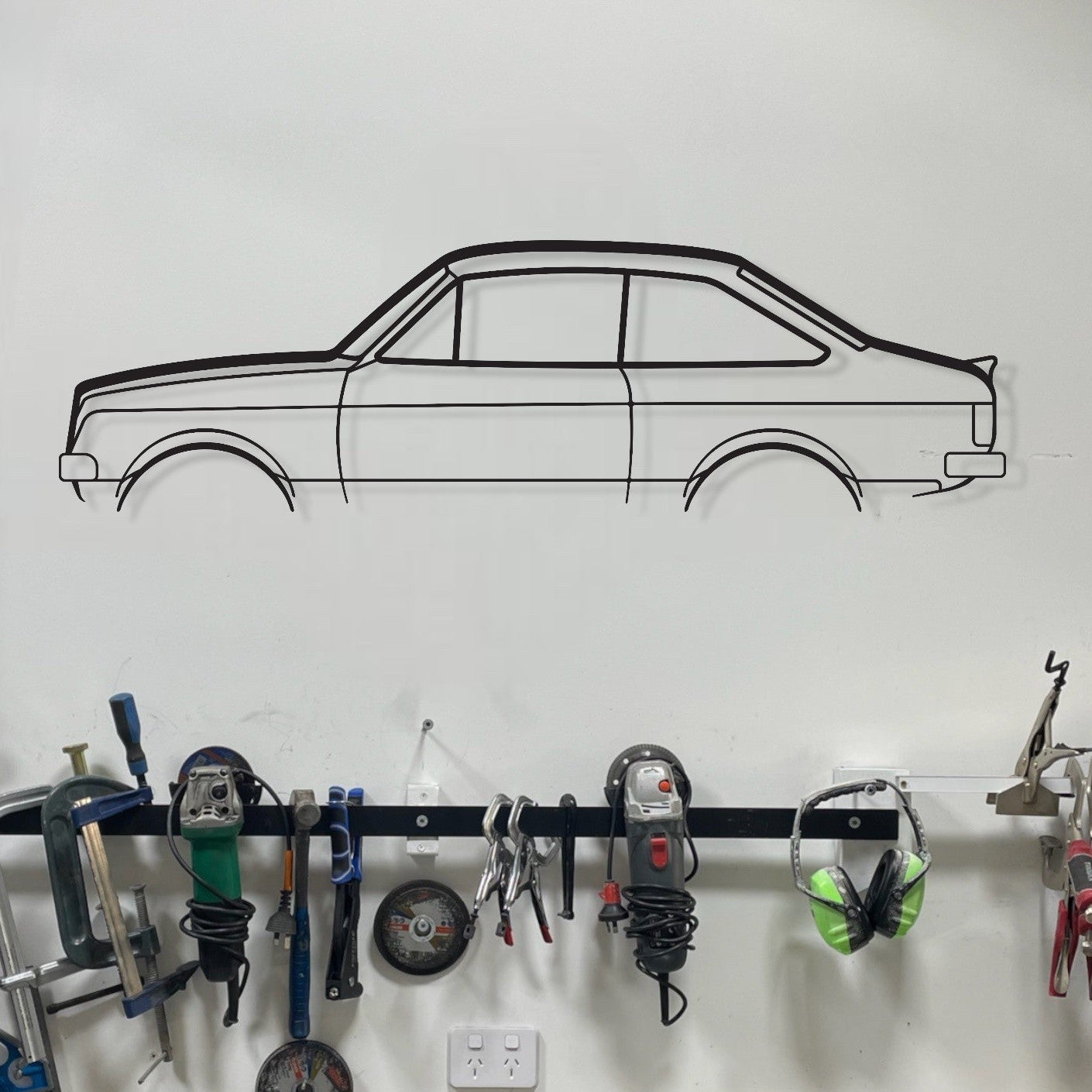Wall-mounted tool rack with various tools above a workbench in a garage setting.