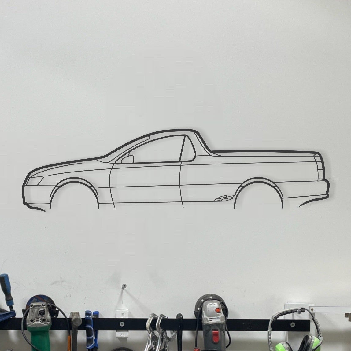 Wall-mounted tool rack with various tools in a garage setting, featuring a car outline on the wall.