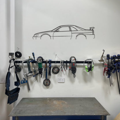 Wall-mounted tool rack with various tools above a workbench in a garage setting.