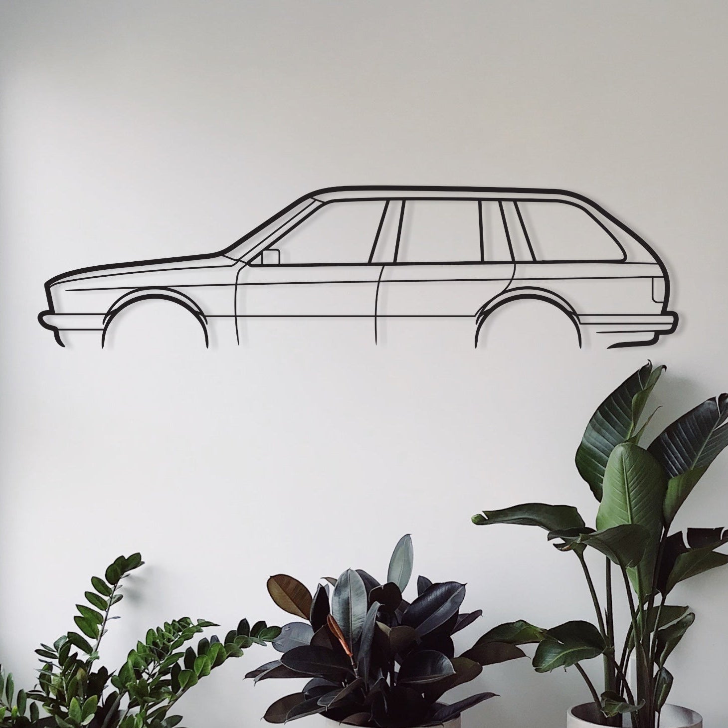A wall-mounted metal silhouette of a BMW E30 Wagon in a room with indoor plants and a patterned rug.